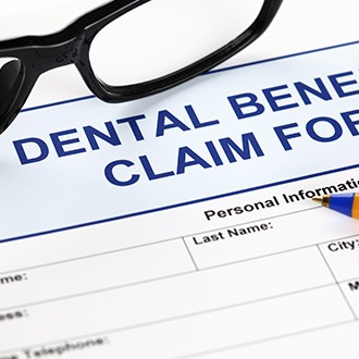 Top of blue Dental Benefits Claim form with pen and black framed glasses