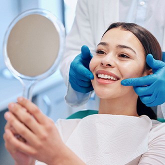 Woman holding mirror in dental chair smiling as dentist points to her teeth