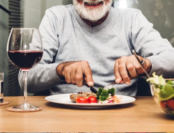 Mouth-down view of a man in grey sweater cutting his chicken and salad with a fork and knife