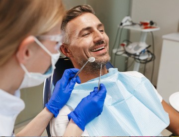 Man with salt-and-pepper beard sitting in dental chair about to undergo an examination