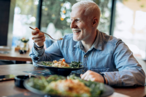 Older man sitting at table holding a forkful of food