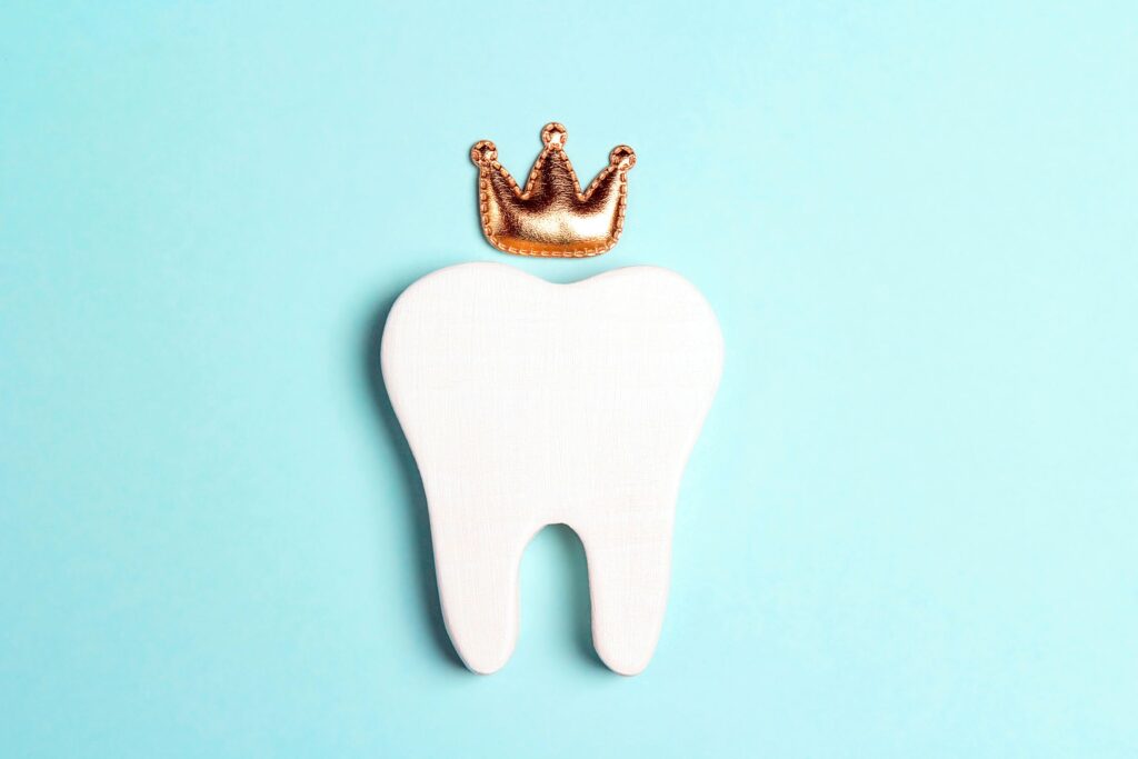 Fake tooth with small crown above it flat on light blue background