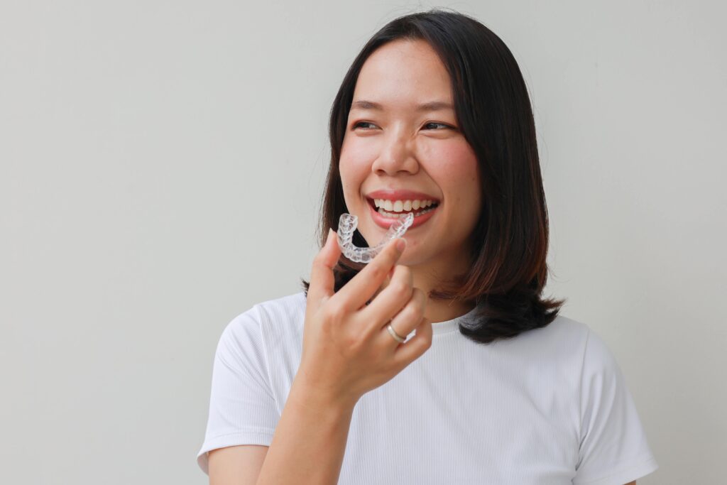 Woman smiling while holding clear aligner